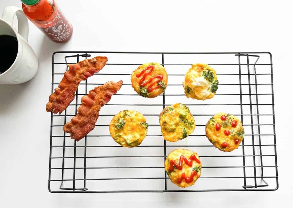 broccoli cheddar egg bites on a wire rack with bacon coffee and hot sauce in the background