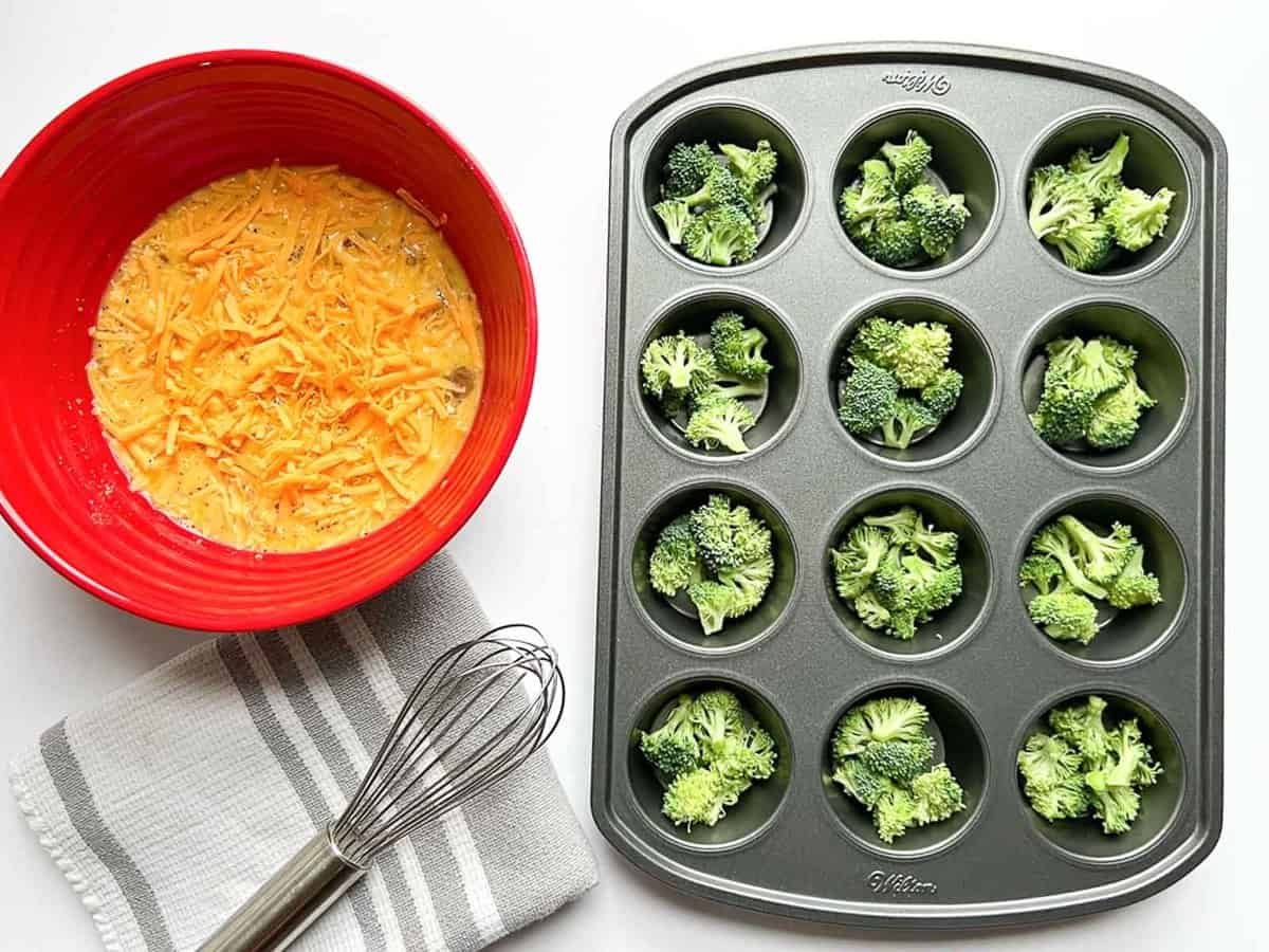 red bowl with egg and cheddar cheese, whisk on grey and white towel, broccoli in muffin tin