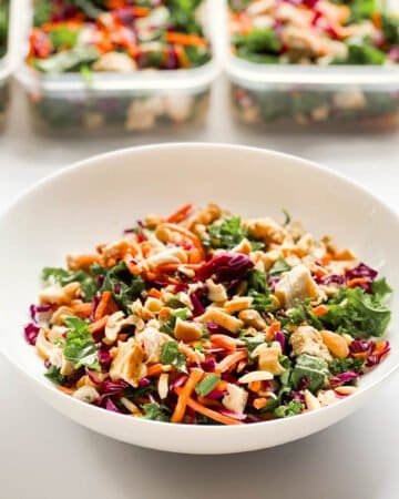 chicken salad in white bowl with chicken salads in containers in background