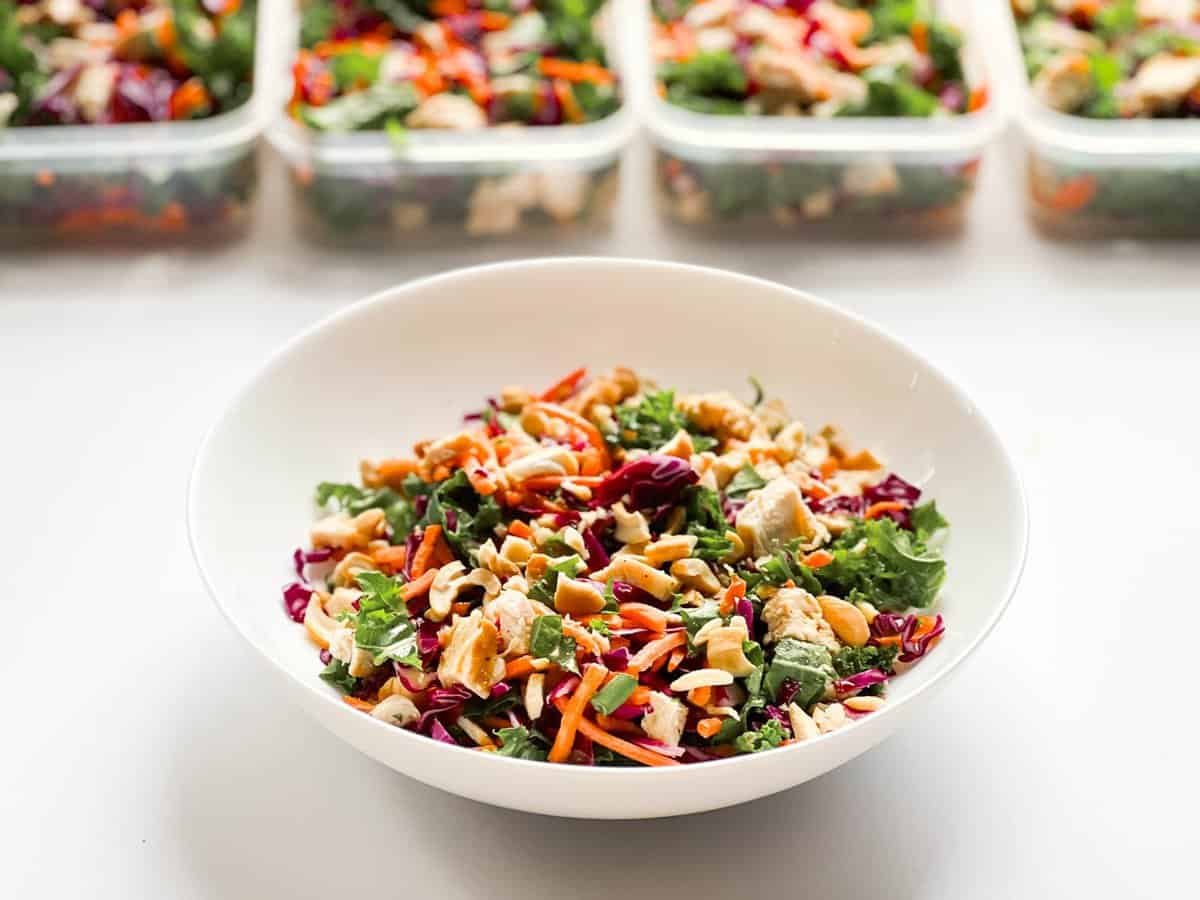 chicken salad in white bowl with chicken salads in containers in background