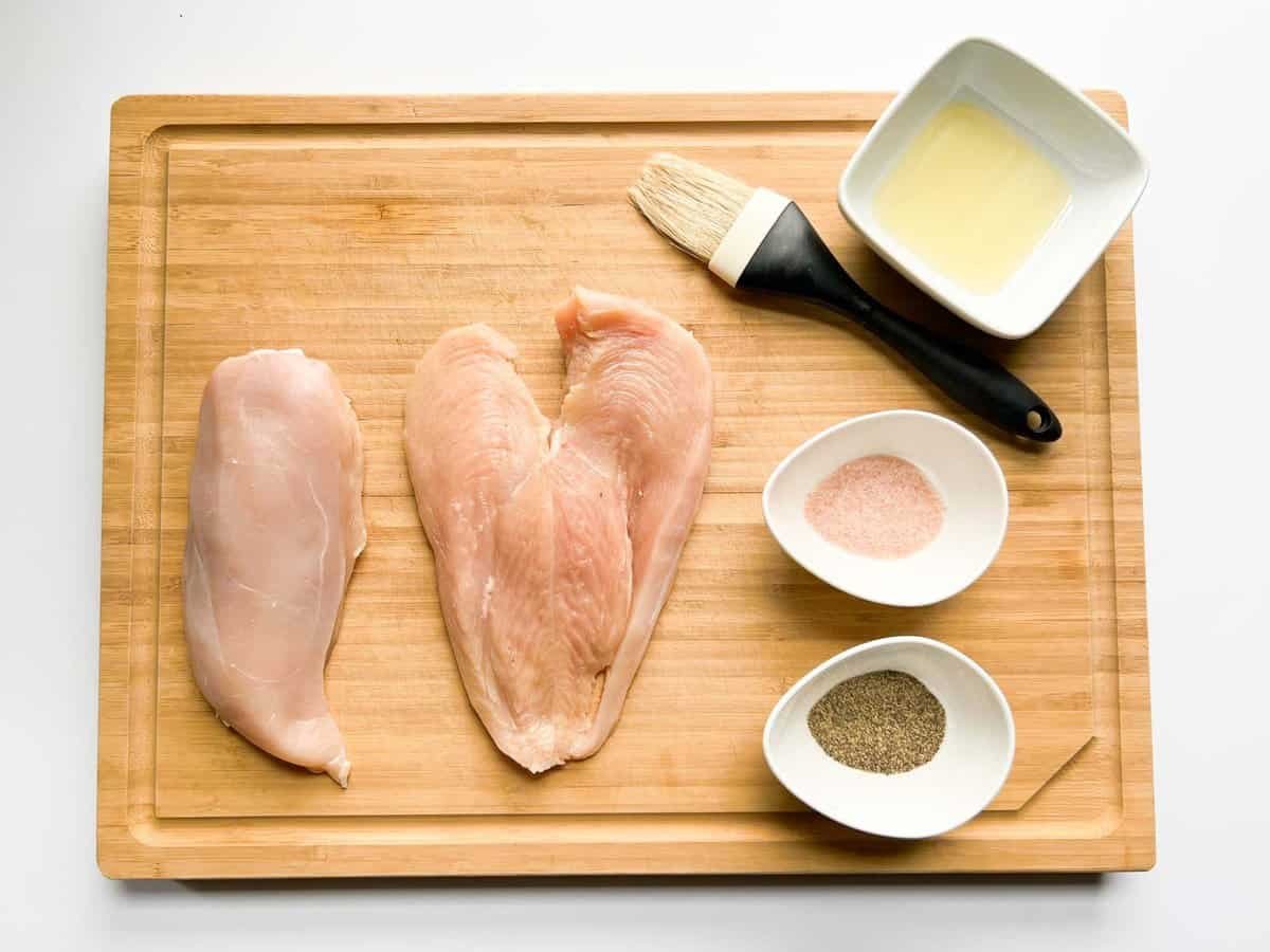 chicken breasts on wooden cutting board with olive oil, salt, pepper on the right