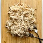 Shredded chicken on wooden cutting board with two forks.