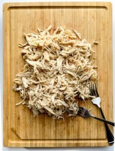 Shredded chicken on wooden cutting board with two forks.